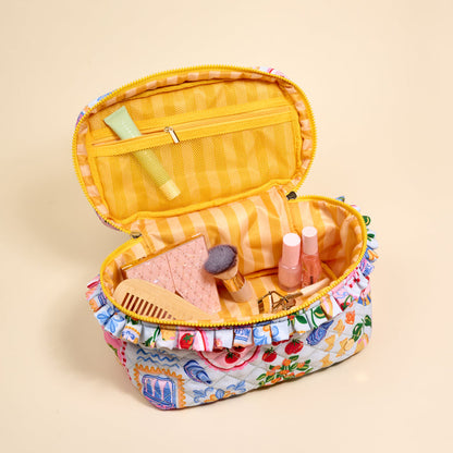 The Darling Effect's Ciao Bella Glam & Go Quilted Cosmetic Bag, featuring a floral pattern and yellow striped interior, is open to reveal cosmetics—a brush, comb, tubes, compact, and a small green tube in the mesh pocket.