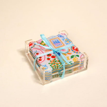 The Darling Effect's Ciao Bella Table Talk Acrylic Coaster Set features vibrant fruit and floral designs. Presented in a clear acrylic holder, these coasters add a cheerful touch to any table setting.