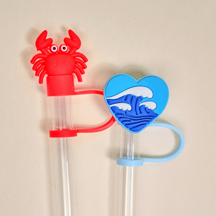 The Darling Effect’s Coast to Coast Straw Topper Set features two clear plastic straws with leak-resistant silicone toppers—a red crab and a blue heart with an ocean wave—that bring playful, mess-free charm to your drinkware.