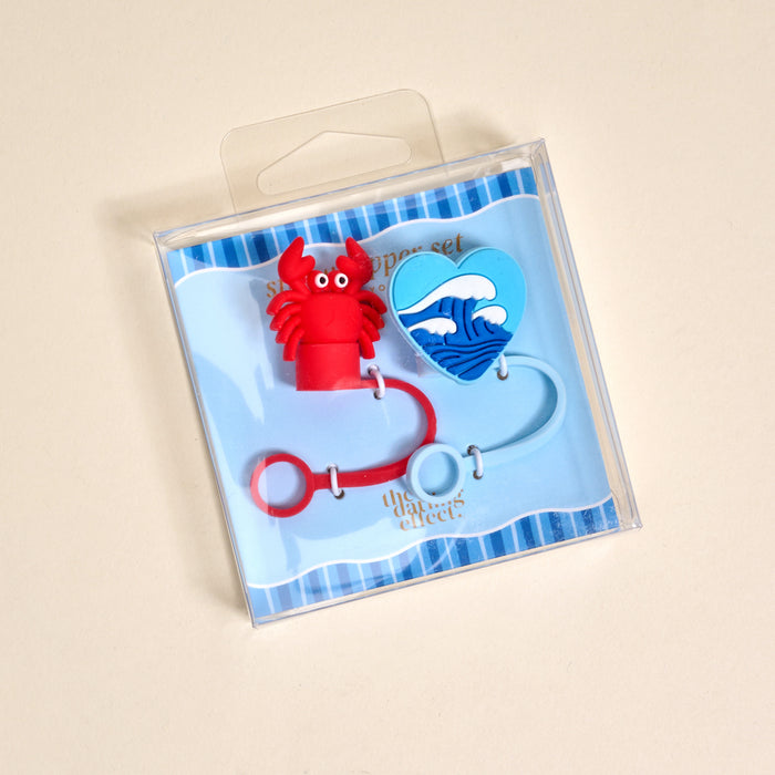 The Darling Effect's Coast to Coast Straw Topper Set includes a red lobster-shaped cable holder and a blue wave-design guitar pick, shown on a blue striped background.