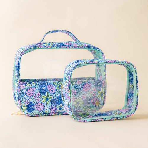 Two clear makeup bags trimmed in a blue, pink, and green floral sea turtle print. This cosmetic bag set includes a larger handled train case and a smaller square pouch, both featuring transparent panels and gold zipper hardware.