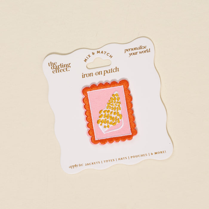 The Darling Effect's Conch Mix & Match Iron-On Patch features a gold embroidered seashell on pink with a red border—ideal for customizing jackets and adding colorful, personal flair.