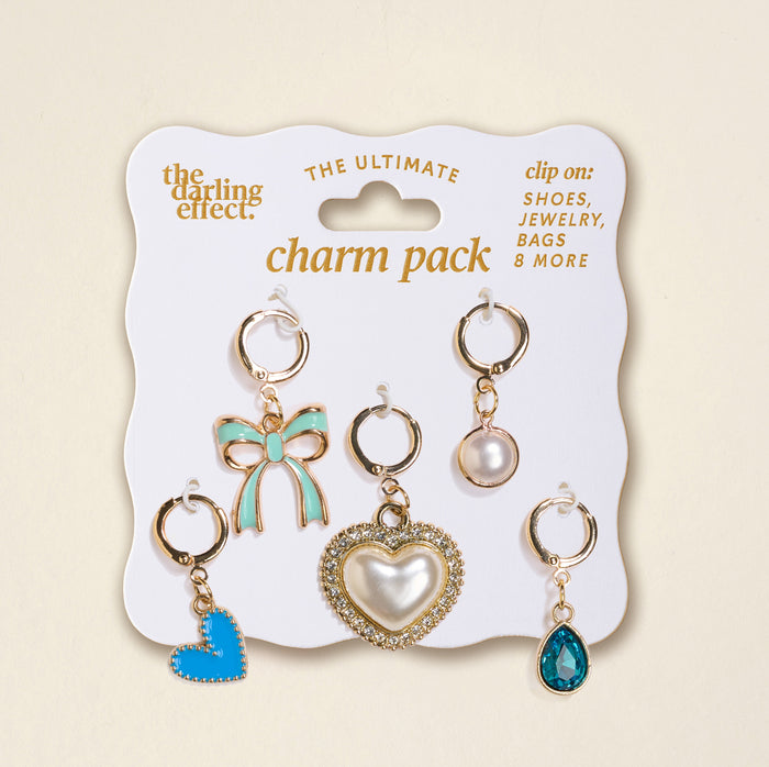 The Darling Effect’s Coquette Cloud The Ultimate Charm Pack features six gold-tone clip-on charms—blue bow, pearl, rhinestone heart, blue heart, clear blue teardrop, and round stone—perfect for scrunchie sets or statement necklaces.
