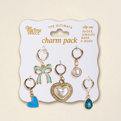 The Darling Effect’s Coquette Cloud The Ultimate Charm Pack features six gold-tone clip-on charms—blue bow, pearl, rhinestone heart, blue heart, clear blue teardrop, and round stone—perfect for scrunchie sets or statement necklaces.