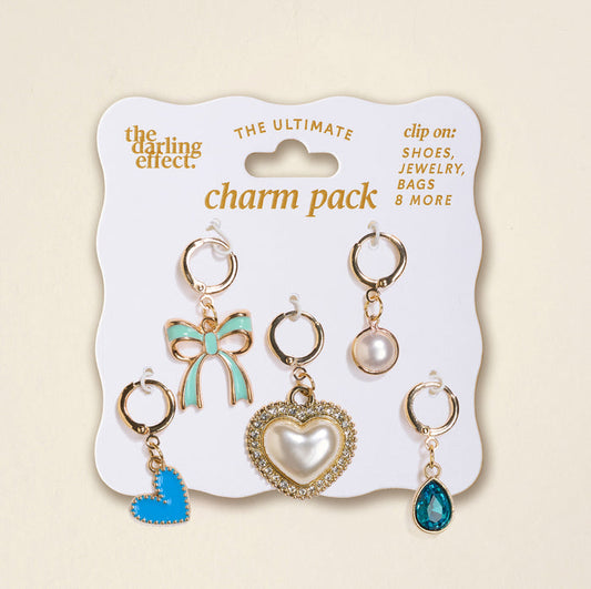 The Darling Effect’s Coquette Cloud The Ultimate Charm Pack features six gold-tone clip-on charms—blue bow, pearl, rhinestone heart, blue heart, clear blue teardrop, and round stone—perfect for scrunchie sets or statement necklaces.