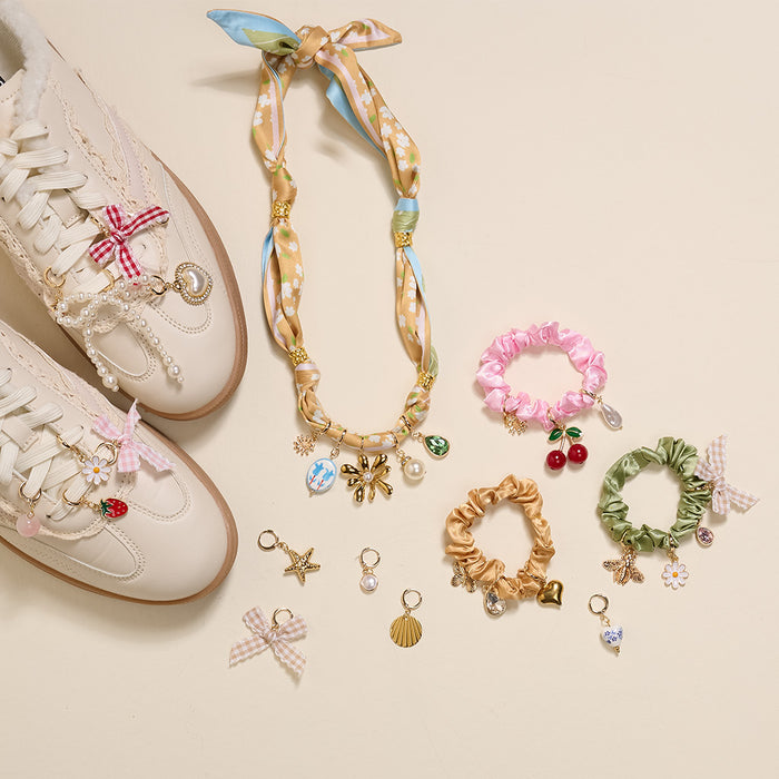 The Darling Effect's Coquette Cloud The Ultimate Charm Pack, featuring white sneakers with lace and charms, a gold and blue statement necklace with charms, and four colorful scrunchie charm sets, is arranged on a light surface.