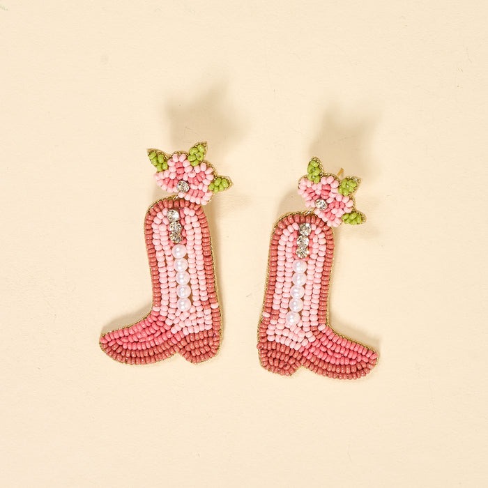 Cowgirl Boot Beaded Earrings by The Darling Effect feature vibrant pink boots with white pearls and green and pink floral beadwork, displayed on a light beige background.