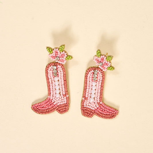 Cowgirl Boot Beaded Earrings by The Darling Effect feature vibrant pink boots with white pearls and green and pink floral beadwork, displayed on a light beige background.