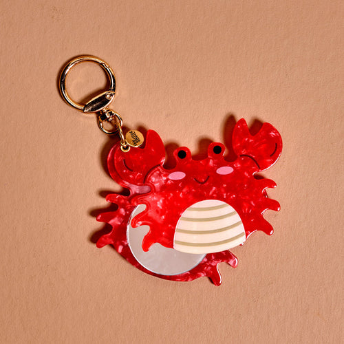 The Darling Effect's Crab Mini Mirror Bag Charm is a shiny red crab keychain with pink cheeks and a smiling mouth, perfect as a cute bag accessory from the Acrylic Mirror Bag Charms collection.