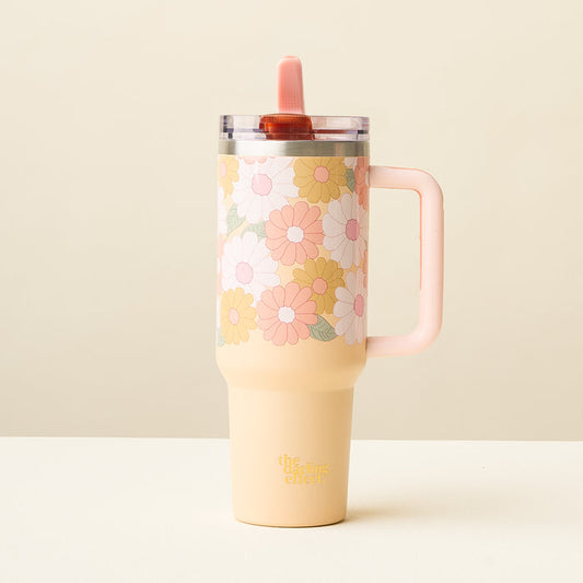 The Daisy Craze Peach 40 oz Lifestyle Flip Straw Tumbler by the-darling-effect features a retro floral pattern in pink, white, and yellow, a pink handle, and a clear leak-resistant flip straw lid with a matching pink straw.