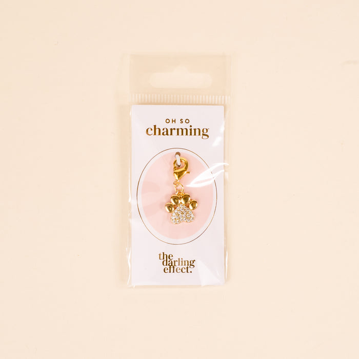 The Darling Effect's Dazzled Paw Print Jewelry Charm Gold features a rhinestone-studded paw design on an OH SO charming card, packaged in a clear sleeve—perfect for adding sparkle to any charm bar collection.