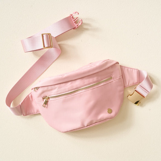 The Darling Effect Dusty Blush XL All You Need Belt Bag, featuring a gold zipper and buckle, rests on a cream background.