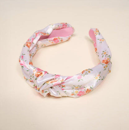 The Darling Effect’s Endless Daydream Cream Classic Twist Headband features a floral print with a chic knot design, shown on a light beige background—a versatile accessory perfect for any occasion.