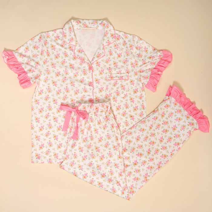 The Darling Effect’s Endless Daydream Cream Slumber Party Pajama Pants Set features a floral print, pink ruffle trim, and soft fabric. Gift-ready set includes a short-sleeved button-up top with chest pocket and matching pants with pink ribbon waistband.