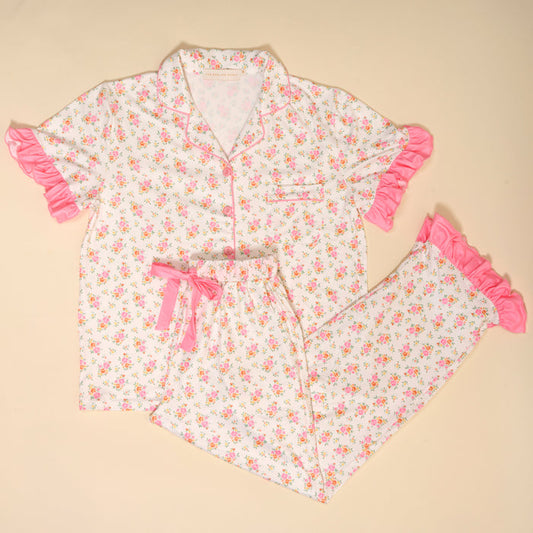 The Darling Effect’s Endless Daydream Cream Slumber Party Pajama Pants Set features a floral print, pink ruffle trim, and soft fabric. Gift-ready set includes a short-sleeved button-up top with chest pocket and matching pants with pink ribbon waistband.