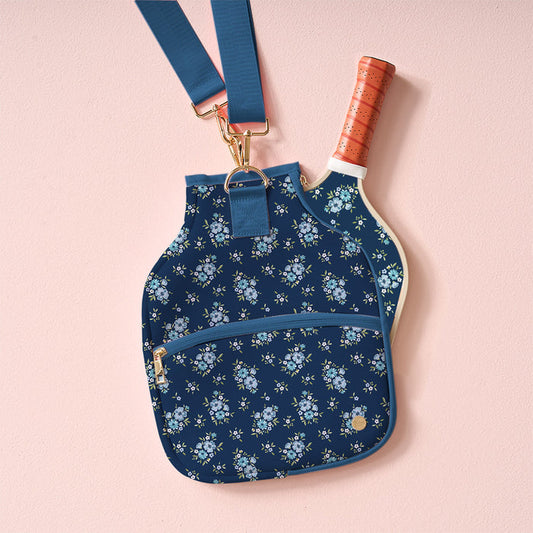 The Endless Daydream Navy Pickleball Paddle Case by the-darling-effect, featuring a floral print and blue strap, is displayed on a pink background—perfect for carrying your pickleball paddles.