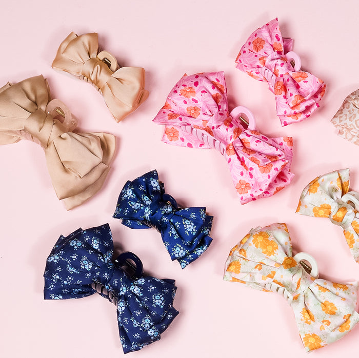 The-darling-effect’s Endless Daydream Navy Satin Bow Claw Clip adds elegance to any updo with its satin bow detail, available in assorted prints and colors like solid beige, pink floral, navy floral, and light green floral with orange flowers.