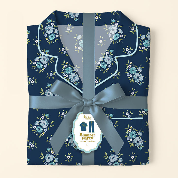 Folded Endless Daydream Navy Slumber Party Pajama Pants Set by The Darling Effect, featuring a light blue and white floral print on ultra-soft fabric, tied with a satin ribbon. Tag displays product name and a relaxed fit illustration.