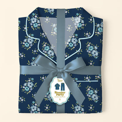 Folded Endless Daydream Navy Slumber Party Pajama Pants Set by The Darling Effect, featuring a light blue and white floral print on ultra-soft fabric, tied with a satin ribbon. Tag displays product name and a relaxed fit illustration.