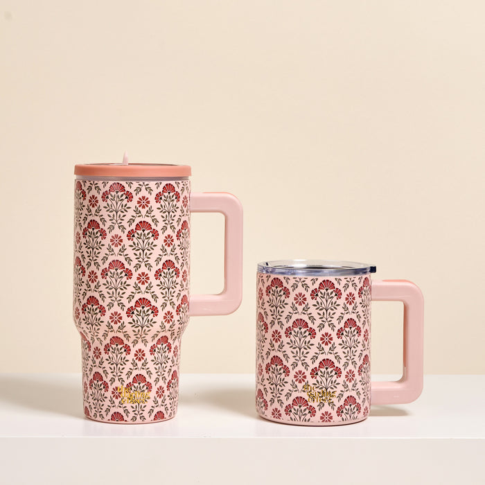 Two Everbloom Dusty Rose 14 oz Insulated Mugs by The Darling Effect, with pink finish, handles, and a floral pattern in red, black, and green, sit side by side on a white surface; the left mug is taller and has a lid.
