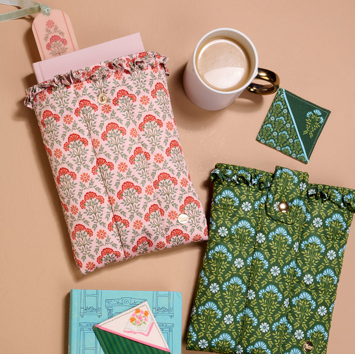 The Everbloom Forest Green Book Cover by The Darling Effect lies on a tan surface with notebooks, envelopes, and coffee nearby, offering charming floral style and ruffled edges for cute book protection.