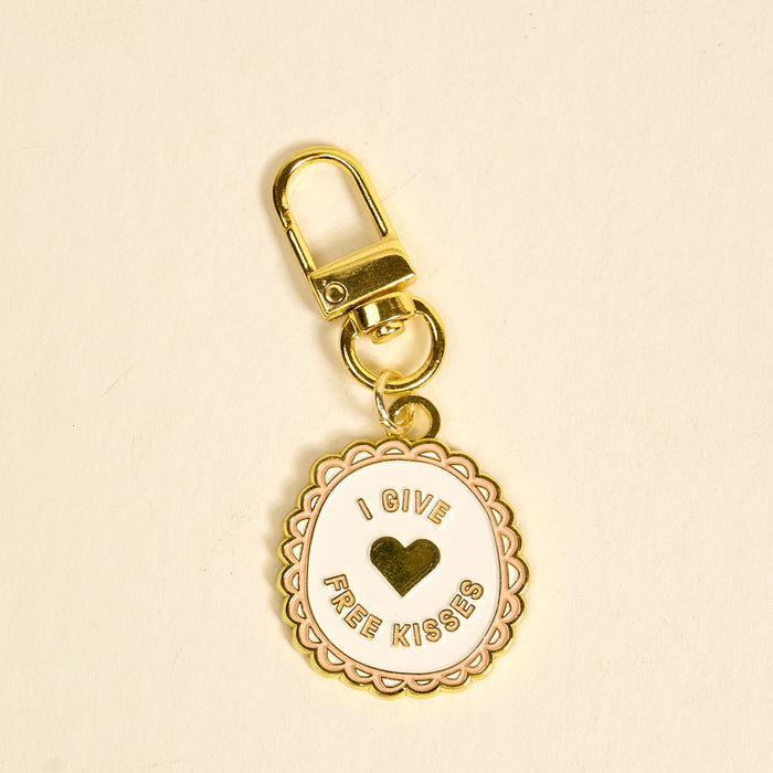 The Darling Effect's Free Kisses Pawfect Collar Charm features a gold, scalloped-edge charm with "I GIVE FREE KISSES" around a gold heart—an adorable accessory to add playful style to your pet’s collar or charm collection.