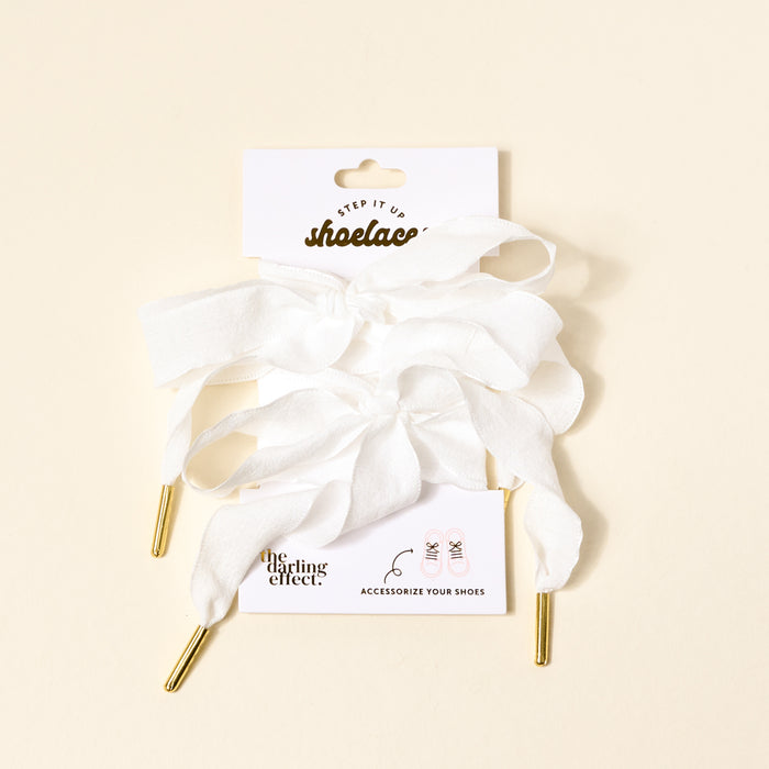 Frilly White Step It Up Shoelaces by The Darling Effect—white, durable laces with gold aglets—attached to a branded card reading "shoelaces" and "ACCESSORIZE YOUR SHOES," displayed on a light beige background.