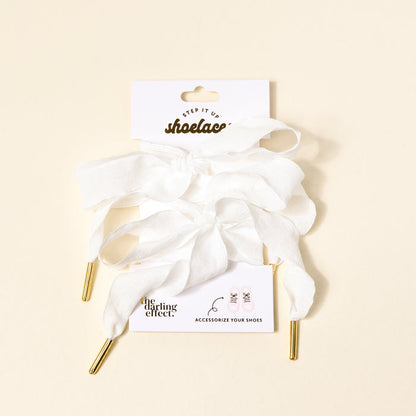 Frilly White Step It Up Shoelaces by The Darling Effect—white, durable laces with gold aglets—attached to a branded card reading "shoelaces" and "ACCESSORIZE YOUR SHOES," displayed on a light beige background.