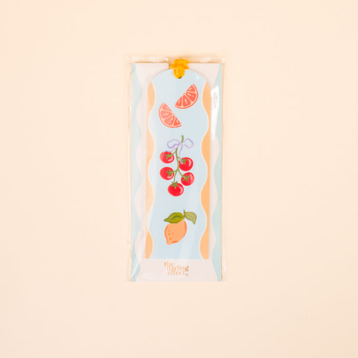 The Darling Effect’s Fruit Market Acrylic Bookmark features vibrant grapefruit, tomato, and pear illustrations—perfect for book lovers or gifting—presented in a clear sleeve on a light beige background.