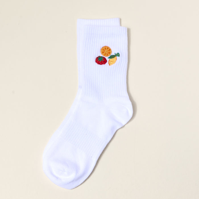 The Darling Effect Fruit Market Embroidered Crew Socks are white with orange slice, strawberry, and lemon wedge designs near the top, shown on a plain light background.