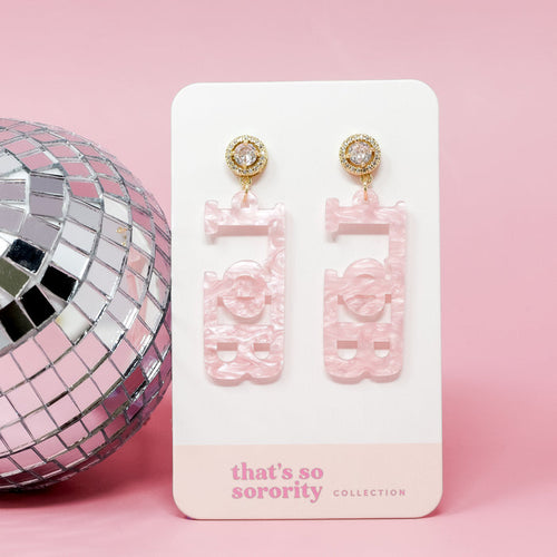 A pair of Gamma Phi Beta Letter Pink Acrylic Earrings by The Darling Effect, featuring gold and rhinestone studs, displayed on a "that's so sorority collection" card beside a silver disco ball—perfect for sisterhood events or bid-day baskets.