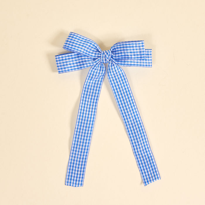 The Darling Effect’s Gingham Blue Double Take Hair Bow features blue and white gingham in a classic bow with two long tails, perfect for hair accessories. Shown on a plain beige background.