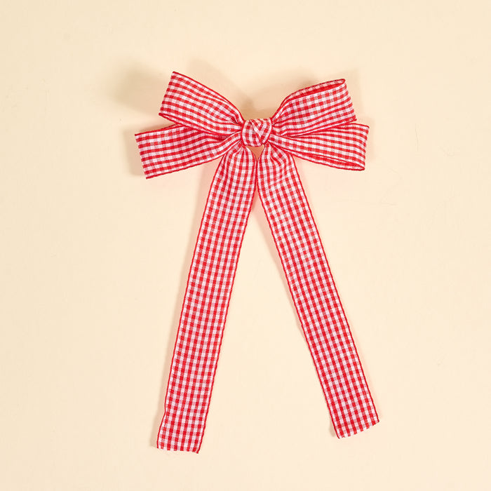 The Darling Effect's Gingham Red Double Take Hair Bow features a red and white checkered ribbon tied into a bow with two long tails, perfect for hair accessories or clips, shown on a plain beige background.