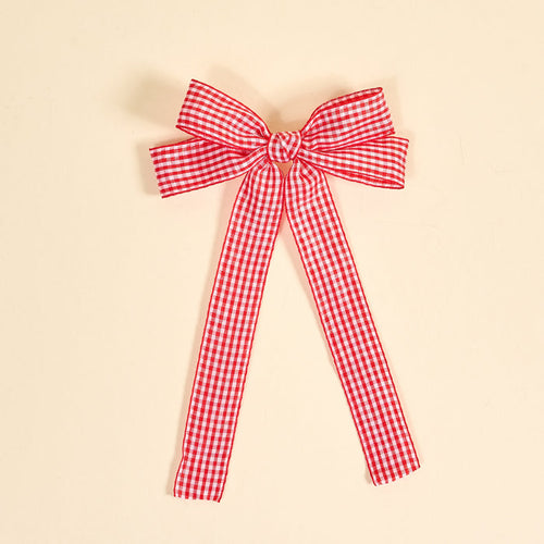 The Darling Effect's Gingham Red Double Take Hair Bow features a red and white checkered ribbon tied into a bow with two long tails, perfect for hair accessories or clips, shown on a plain beige background.
