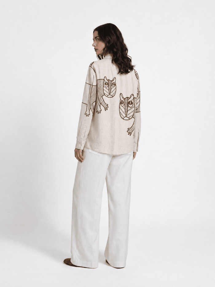 Woman wearing the off white Gond Tiger shirt with white trousers, full length back view, looking over her shoulder