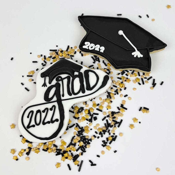 Two black-and-white cookies placed side by side: one shaped like a black graduation cap with a white tassel and "2022" written in white, and the other featuring "Grad 2022" writing in black on a white background.
