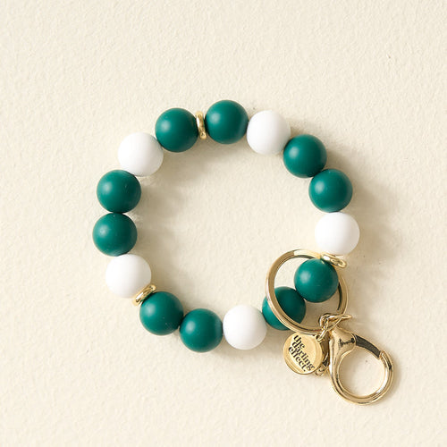 The Darling Effect Green Gameday Hands-Free Keychain Wristlet features alternating green and white beads, gold rings, a lobster clasp, and a round charm engraved with “Simply Southern”—perfect for showing off your school colors.