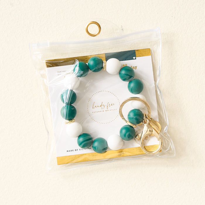 The Darling Effect Green Gameday Hands-Free Keychain Wristlet includes a green and white beaded bracelet, gold keyring, and “hands free” card in a clear pouch with top grommet for hanging.