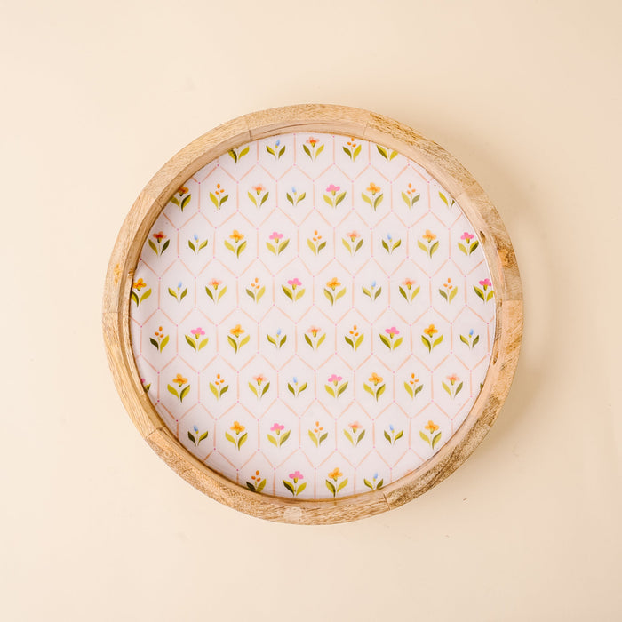 The-darling-effect’s Handpicked For You Large Round Wood Enamel Tray features a white base with colorful floral and green leaf patterns, set against a light beige background for a decorative touch.