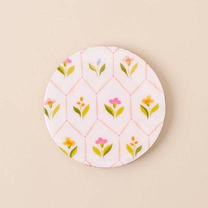 A round ceramic plate with a white background and pastel floral pattern is paired beautifully with the-darling-effect's Handpicked for You Wood Enamel Coaster on a beige surface.