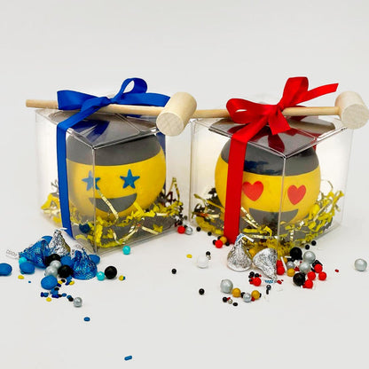 Two chocolate happy faces, one with blue start eyes and the other with red heart eyes, both wearing a graduation caps. Each is in a clear box. The boxes are wrapped with a blue and red bows and a mallet. Assorted candies are spread on the outside to show the content. There are two options: blue and red.