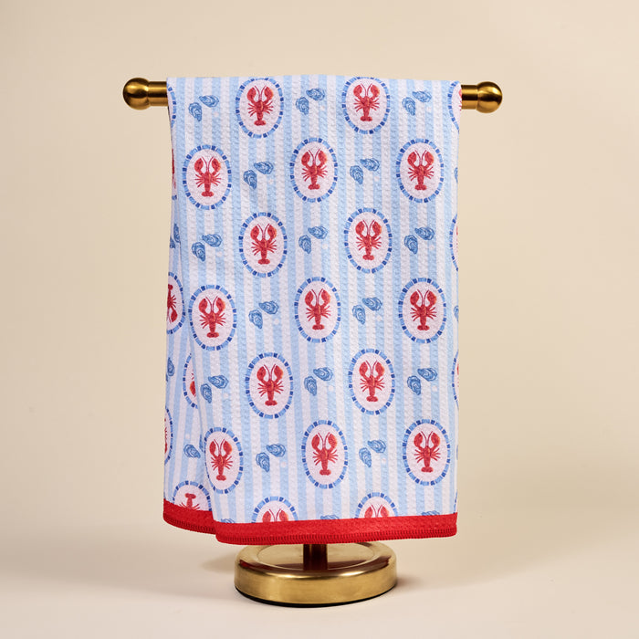 The Darling Effect’s Harbor House Waffle Tea Towel, featuring red lobsters and blue shells with vertical stripes and a red border, brings coastal charm and absorbency to your kitchen decor.