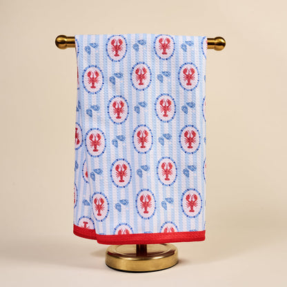 The Darling Effect’s Harbor House Waffle Tea Towel, featuring red lobsters and blue shells with vertical stripes and a red border, brings coastal charm and absorbency to your kitchen decor.