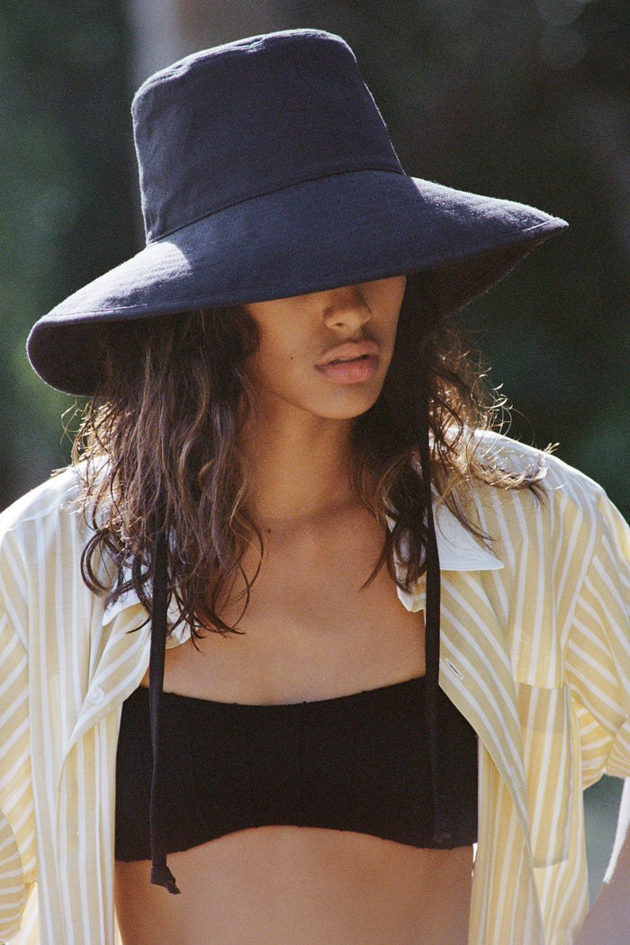 Model wearing a black cotton bucket hat with neck tie, styled with a striped shirt and bikini top