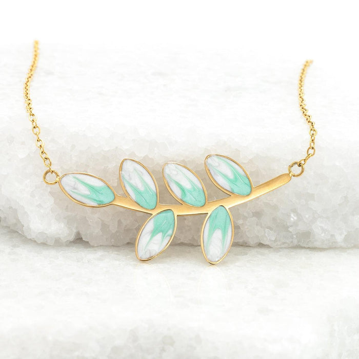 Gold necklace with mint enamel leaves on a white marble background
