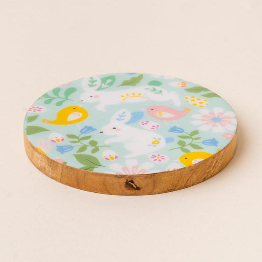 The-darling-effect's Hoppy Days Wood Enamel Coaster features white bunnies, yellow birds, pink flowers, and green leaves on light blue—combining style and function to brighten your table with a charming decorative touch.