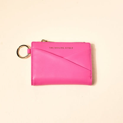 The Darling Effect’s Hot Pink Luxe Pocket Wallet is a vegan leather wallet with gold zipper and keyring, featuring “THE DARLING EFFECT” in gold on the front—an everyday essential shown against a light beige background.