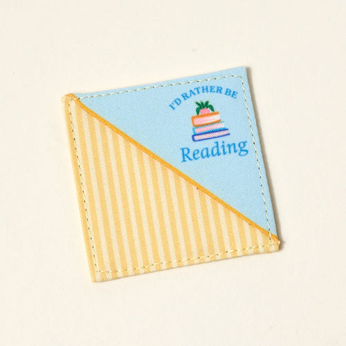 The Darling Effect’s "I'd Rather Be Reading" Corner Keeper Fabric Bookmark features diagonal yellow stripes, solid blue, a book stack, and text—perfect for book lovers.