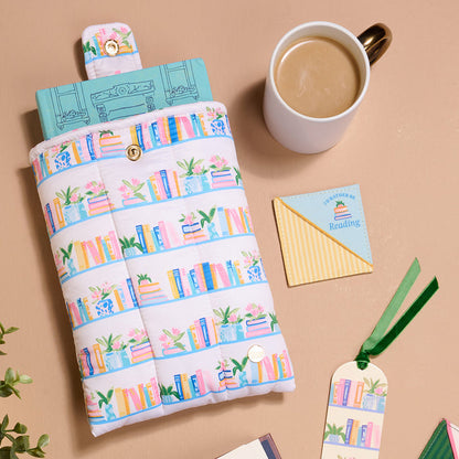 The Darling Effect’s "I’d Rather Be Reading" Corner Keeper Fabric Bookmark is displayed on a tan surface with a book-themed pouch, coffee, a “Sssh! I'm reading” note, another fabric bookmark, and green leaves—a perfect gift for book lovers.