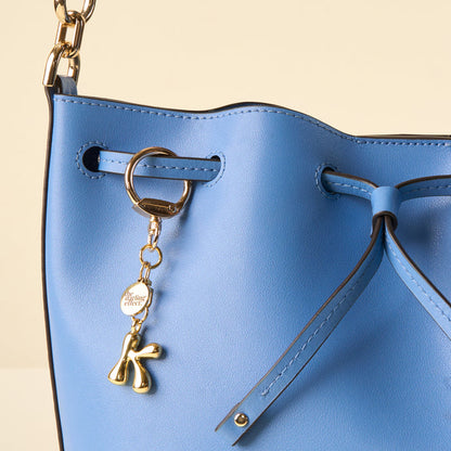 A close-up of a blue leather bucket bag features the-darling-effect's K Bubble Letter Keychain Bag Charm and a darling effect tag.